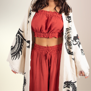 Woman wearing the Red Dragon Kimono – ivory organic cotton kimono with bold black dragon design, styled over a rust-colored two-piece set.