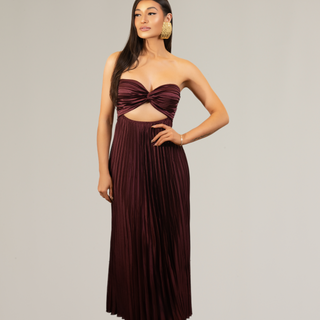 Woman wearing the Pillar Twist Front Dress in burgundy – strapless pleated satin gown with twist-front bodice and center cutout.