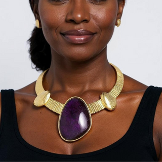 Woman wearing the Purple Rain Statement Necklace with sleek black top, showcasing a bold purple gemstone and gold collar.

